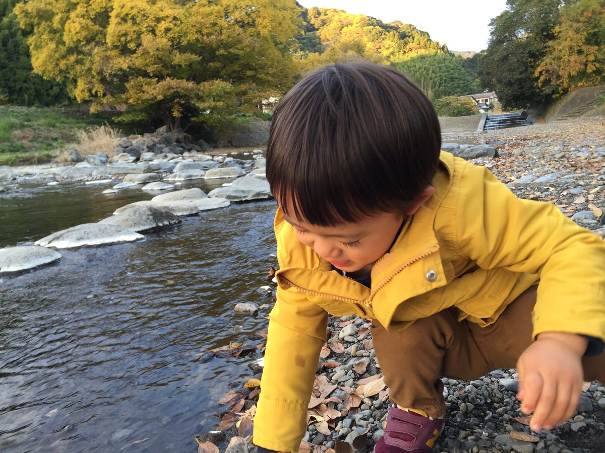 川原にしゃがんで石を触る2歳の上の子